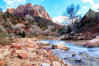 Arka planda bir dağ olan bir nehir bir kanyonun içinden akar. Su temiz ve kayalar tüm bölgeye dağılmış durumda. Huzurlu ve huzurlu bir sahne.