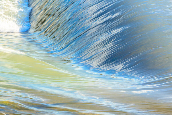 Волна врезается в берег, вода отражает небо и солнце. Сцена спокойная и мирная, так как вода, кажется, находится в состоянии постоянного движения