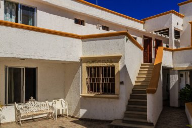 Balkonlu ve banklı beyaz bir bina. Balkonda şöyle bir tabela var: