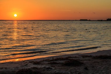 Güneş okyanusun üzerinde batıyor, suyun üzerine sıcak bir parıltı saçıyor. Gökyüzü turuncu ve pembe renklerin bir karışımıdır. Huzurlu ve huzurlu bir atmosfer yaratır. Kumsal çok sessiz.