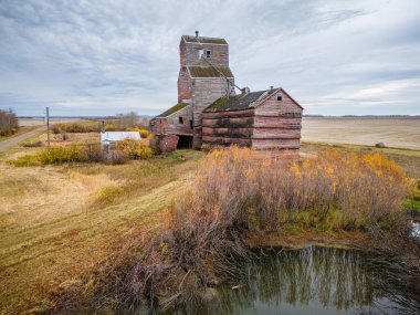 Önünde gölet olan bir tarlada büyük, eski bir bina oturuyor. Bina tahıl ambarı gibi görünüyor ve gölet uzun otlarla çevrili.