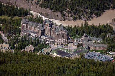 Arkasında bir sürü ağaç olan büyük bir otel. Otel bir ormanla çevrili ve içinden bir nehir akıyor.
