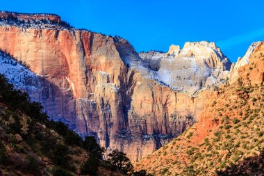 Tepesinde kar ve arka planında mavi bir gökyüzü olan bir dağ sırası. Dağlar kırmızı ve kahverengidir