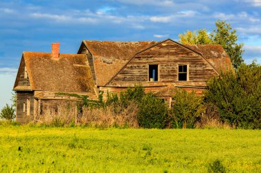 Büyük, eski bir ev bir çim tarlasında duruyor. Ev ağaçlardan ve çalılardan oluşan bir çalılıkla çevrilidir. Gökyüzü bulutlu ve güneş gökyüzünde alçalır.