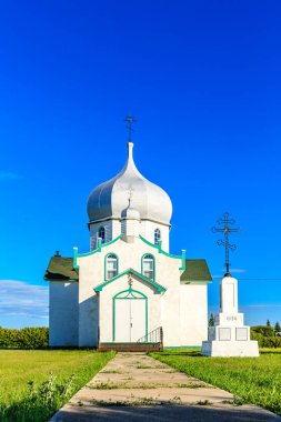 Yeşil çatılı ve üzerinde haç olan küçük beyaz bir kilise. Kilise çimenlik bir alanla çevrilidir.