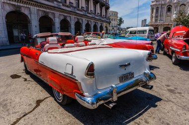 Bir binanın önünde kırmızı ve beyaz bir araba park edilmiştir. Araba bir klasik ve beyaz bir plakası var.