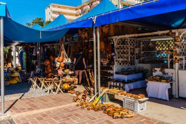 Bir mağazanın önünde mavi tenteli mavi bir çadır kuruluyor. Dükkan ahşap eşyalar satıyor ve bir kadın yürüyor.