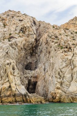 Ortasında küçük bir mağarası olan kayalık bir uçurum. Uçurum çok yüksek ve su sakin.