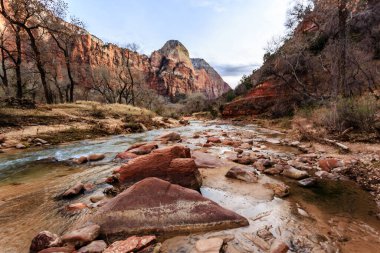 Kayalık bir kıyı şeridi ve arkasında dağlar olan bir nehir. Su berrak ve kayalar kahverengi.