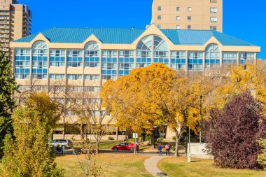 Önünde mavi bir çatı ve kırmızı bir araba olan büyük bir bina. Binanın bir sürü penceresi ve büyük bir otoparkı var.