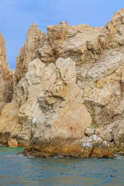 Arka planda mavi gökyüzü olan kayalık bir uçurum. Uçurum beyaz ve kahverengi kayalarla kaplıdır.