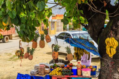 İçinde muz, ananas ve elma olan bir meyve standı. Tribünün önüne beyaz bir araba park etmiş.