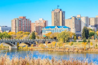Üzerinden bir nehir akan ve üzerinde bir köprü olan bir şehir. Binalar yüksek ve gökyüzü mavi.