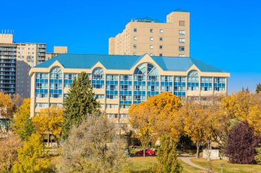 Mavi çatılı ve pencereli büyük bir bina. Bina ağaçlar ve bir parkla çevrili.