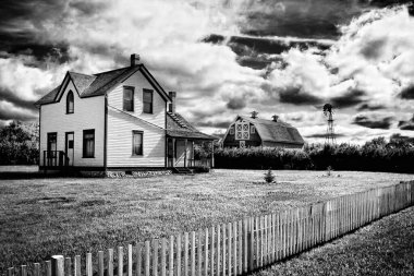 Bir ev ve çitin siyah beyaz fotoğrafı. Ev eski ve çit ahşap. Manzara nostaljik ve huzurlu.