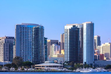 Ortasında büyük bir bina olan bir şehir silueti. Gökyüzü açık ve mavi. Binalar uzun ve parlak.