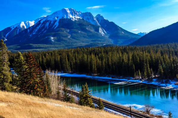 A beautiful mountain range with a river running through it. The water is clear and calm, reflecting the mountains in the distance. The scene is peaceful and serene, with the mountains