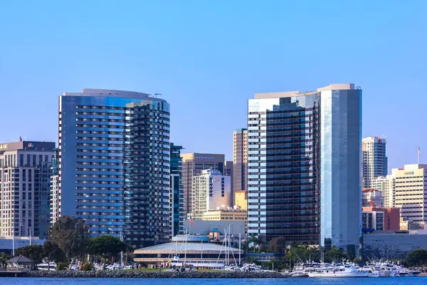 Ortasında büyük bir bina olan bir şehir silueti. Gökyüzü açık ve mavi. Binalar uzun ve parlak.