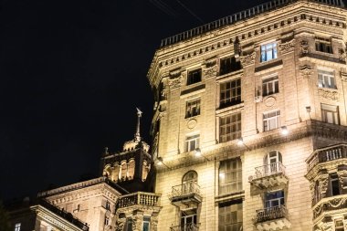 Bir sürü penceresi ve balkonu olan büyük bir bina. Bina gece aydınlanıyor.