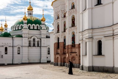 Bir kadın yeşil kubbeli bir kilisenin önünden geçiyor. Kilisenin etrafı kaldırımı kaldırımlı bir avluyla çevrili.