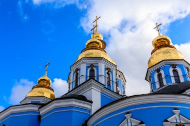 Mavi ve altın kilisenin tepesinde üç kubbe ve haç var. Gökyüzü mavi ve bulutlar beyaz