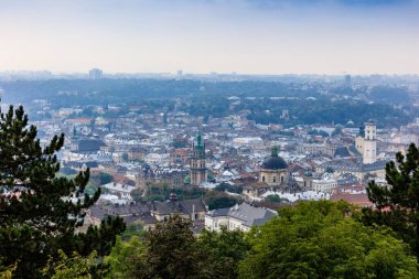 Bir sürü bina ve ağaçla dolu bir şehir manzarası. Gökyüzü bulutlu ve şehir huzurlu görünüyor.
