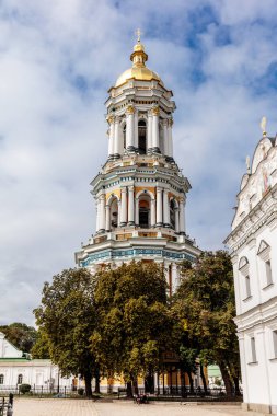 Üzerinde altın kubbe ve mavi-beyaz haç olan uzun beyaz bir bina. Bina ağaçlarla çevrili ve önünde bir avlu var.