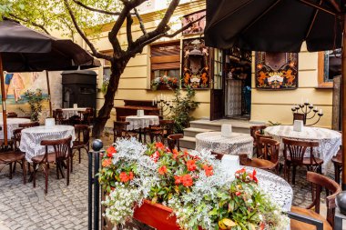 Masaları ve sandalyeleri olan bir restoran terası ve ortasında kırmızı çiçekler olan büyük bir saksı bitkisi.