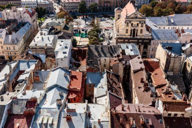 Bir sürü binası ve kilisesi olan bir şehir manzarası. Binalar yüksek ve çatıları var. Gökyüzü mavi ve güneş parlıyor.