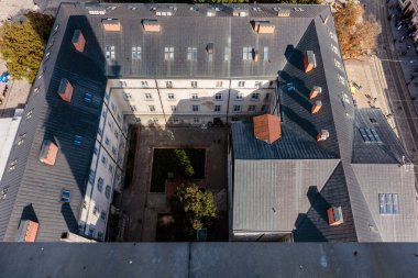 Ortası avlusu olan bir bina ve bacası olan bir çatı. Çatı kiremitlerle kaplı ve binanın bir sürü penceresi var.