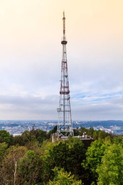 Ormanın ortasında kırmızı tepeli uzun bir kule duruyor. Kule ağaçlarla çevrili ve o bir radyo kulesi. Gökyüzü bulutlu ve ağaçlar yeşil