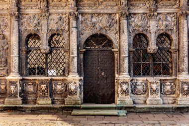 Büyük kapısı ve penceresi olan bir bina. Kapı ahşaptan yapılmış ve bir kilidi var. Bina eski ve üzerinde çok fazla detay var.