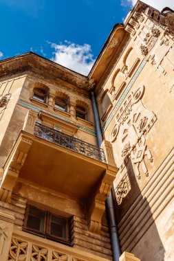 Arka planda mavi gökyüzü ve balkonu olan bir bina. Binanın bir sürü penceresi ve mavi borusu var.