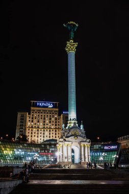 Tepesinde kadın heykeli olan yüksek bir bina. Bina gece aydınlanıyor.