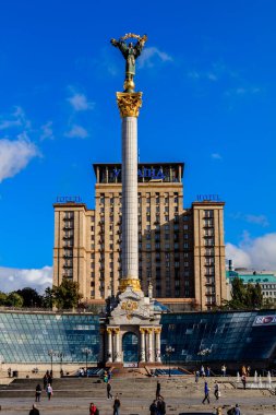 Üzerinde bir kadın heykeli olan yüksek bir bina. Bina büyük bir plazayla çevrili. Etrafta insanlar dolaşıyor.