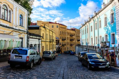 Eski ve yeni binaların karışımı bir cadde ve yolun kenarına park edilmiş birkaç araba.
