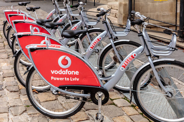 Ряд велосипедов с красной и серебряной рекламой Vodafone. Велосипеды припаркованы на мощеной улице