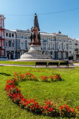 Bir adamın heykeli, büyük kırmızı bir çiçek aranjmanı olan bir binanın önünde duruyor.