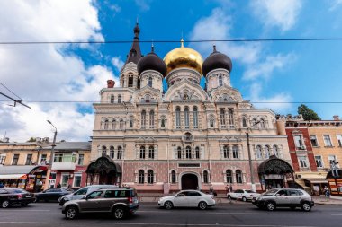 Meşgul bir caddenin önünde altın kubbeli büyük bir bina duruyor. Sokaklar araba ve insanlarla dolu ve gökyüzü açık ve mavi.