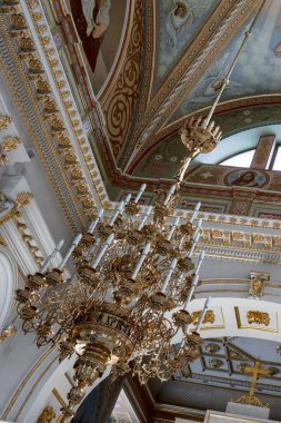 Bir odanın tavanında bir avize asılı. Avize altından yapılmıştır ve üzerinde birçok mum vardır. Oda çok süslü ve bir sürü altın süslemesi var.