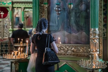 Bir kadın kilisede bir tabloya bakıyor. Siyah bir elbise ve eşarp giyiyor.