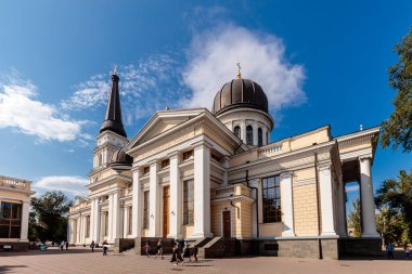 Tepesinde kubbe ve çan kulesi olan büyük beyaz bir bina. Bina bir avluyla çevrili. Etrafta insanlar dolaşıyor.