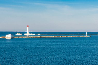 Uzakta bir deniz feneri var ve su sakin. Gökyüzü açık ve mavi