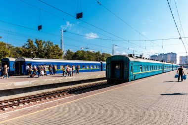 İstasyona mavi trenli bir tren istasyonu geliyor. İnsanlar istasyonda dolanıp treni bekliyor.