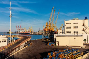 Birçok vinç ve büyük bir binası olan büyük bir sanayi bölgesi. Gökyüzü mavi ve su sakin.