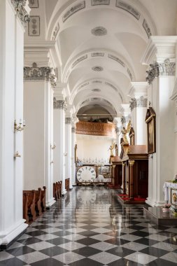 Duvarında saat olan uzun, dar bir oda. Oda ahşap sandalyeler ve banklarla dolu.