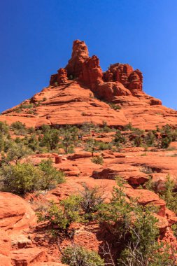 Kırmızı tepeli ve mavi gökyüzü olan bir dağ. Dağ ağaçlar ve çalılarla çevrilidir.