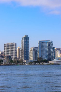 Arka planda büyük bir su kütlesi olan bir şehir silueti. Su sakin ve gökyüzü berrak.