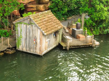 Sudaki bir rıhtımda küçük ahşap bir kulübe duruyor. Kulübe zincirli tel örgülerle çevrili ve ona bağlı küçük bir tekne var. Su sakin ve sahne huzurlu, huzurlu bir ruh haline sahip.