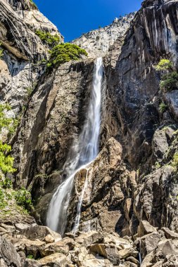 Bir şelale kayalık bir uçurumdan aşağı akıyor. Su berrak ve kayalar pürüzsüz. Sahne huzurlu ve huzurlu.
